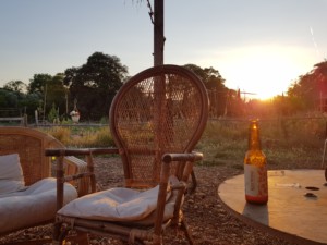 Une chaise en osier vide à côté de laquelle repose une bière prête à être dégustée, sur un magnifique fond de soleil couchant