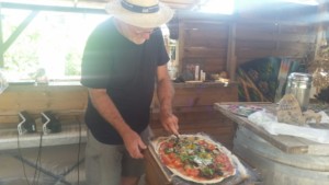 Un homme est en train de préparer une pizza avec des légumes frais dans la cuisine de l'Oasis