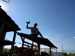 Un homme à contre jour assis sur le toit et brandissant une visseuse