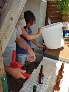 Une personne vide le fond d'un tonneau en plastique blanc dans une canette en verre pendant qu'une autre personne sertit les précédentes canettes d'une capsule métallique.