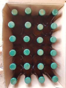 Carton de 24 canettes de bières vues du dessus. Elles sont de couleur brune avec un bouchon vert olive.