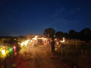 Arche d'entrée de l'Oasis près de laquelle attend une personne dans l'ombre. Le ciel nocturne est d'un bleu profond, criblé d'étoiles.