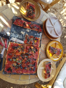 Grande pizza rectangulaire artisanale découpée en belles parts généreuses.