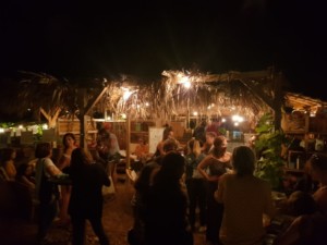 Paillote de nuit, remplie de personnes en train de discuter en petits groupes.