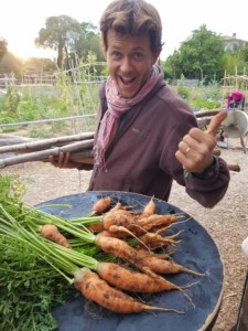 Germain pose le pouce en l'air avec un grand sourire derrière une table couverte de carottes tout juste cueillies.