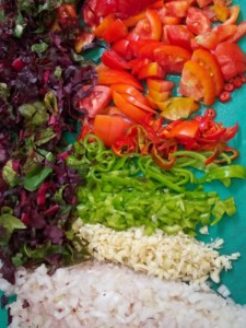 Composants d'une salade composée coupés en morceau et disposés côté à côté sur une planche à découper.